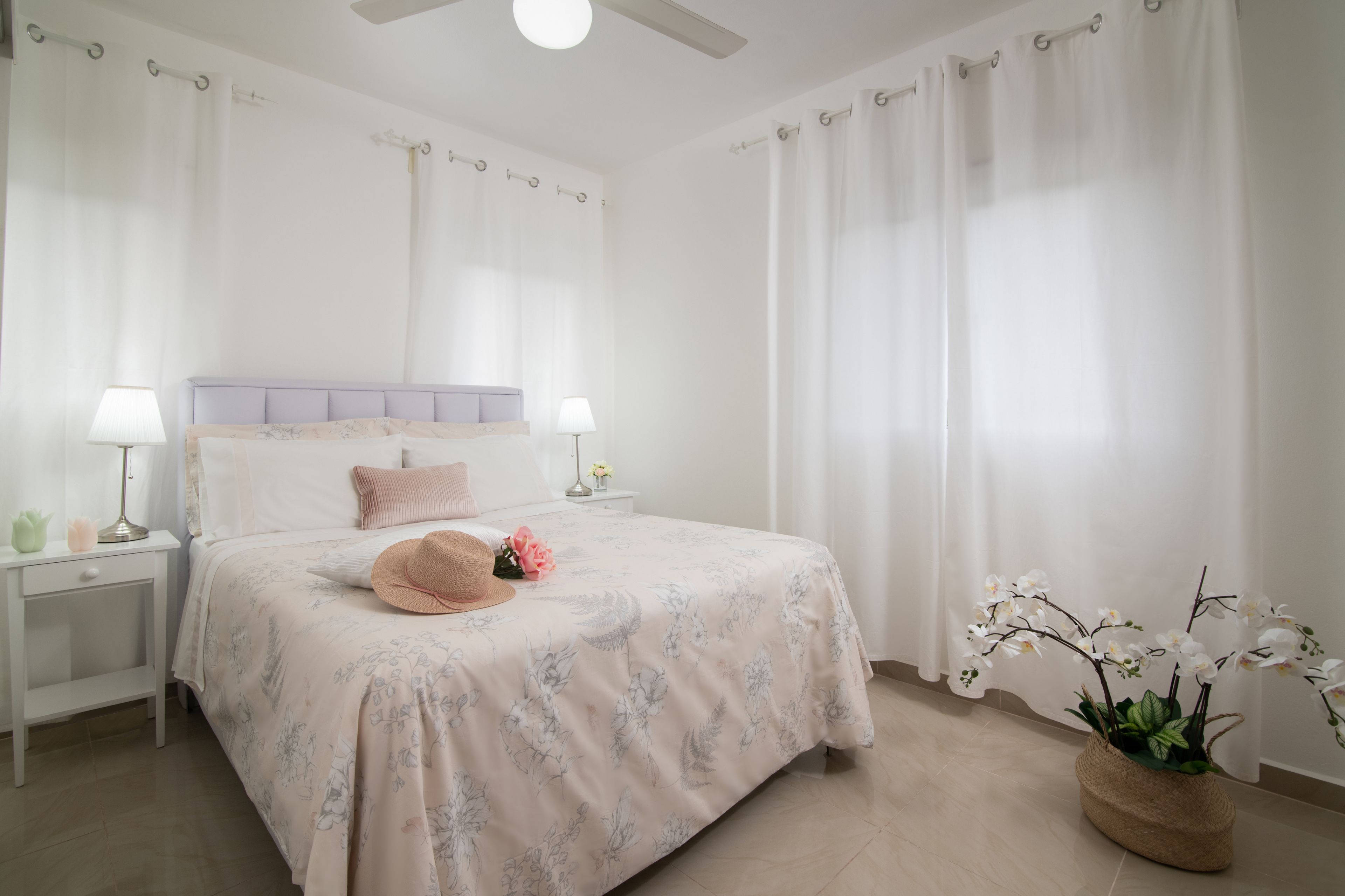 A bedroom with a bed, nightstands, a ceiling fan, and a potted plant.