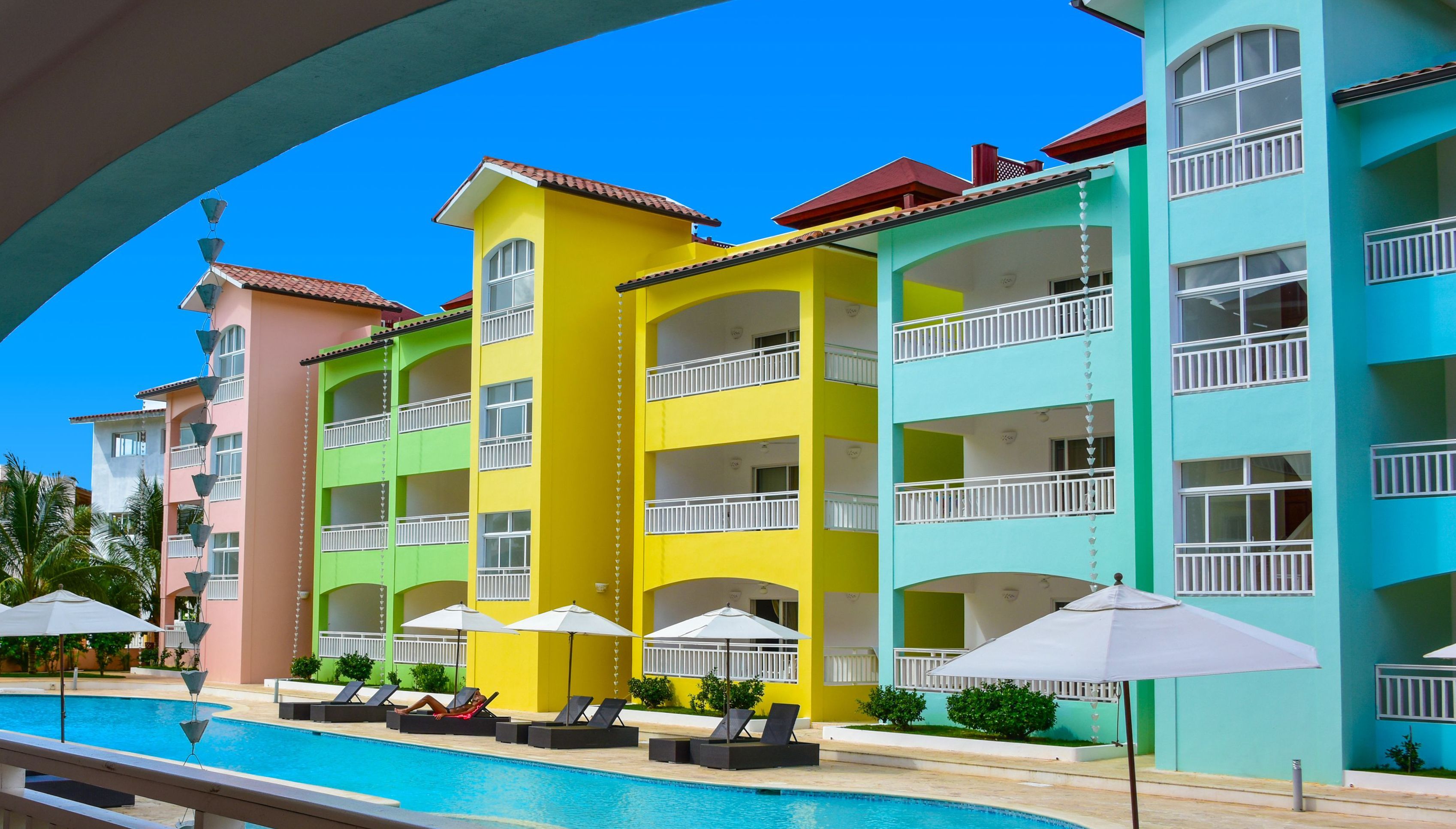 A multi-story hotel with balconies, a swimming pool, and outdoor umbrellas.