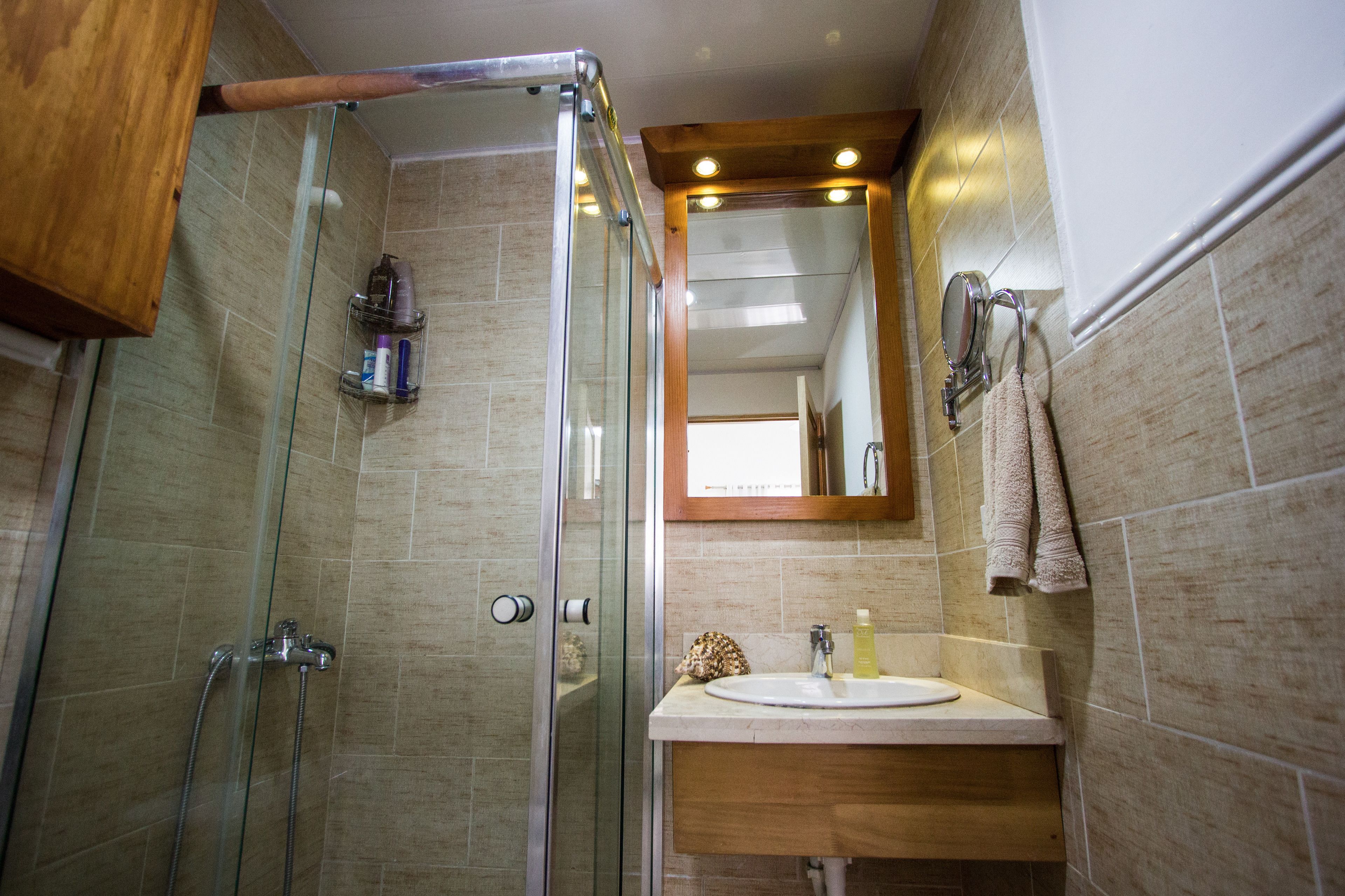 A bathroom with a glass shower enclosure, a sink with a mirror above it, and a towel hanging on the wall.