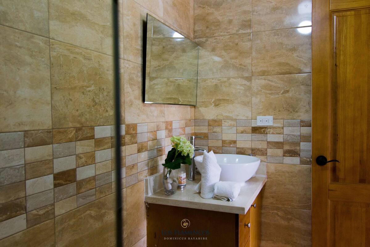 A bathroom with a marble wall, a sink, a mirror, and a wooden door.