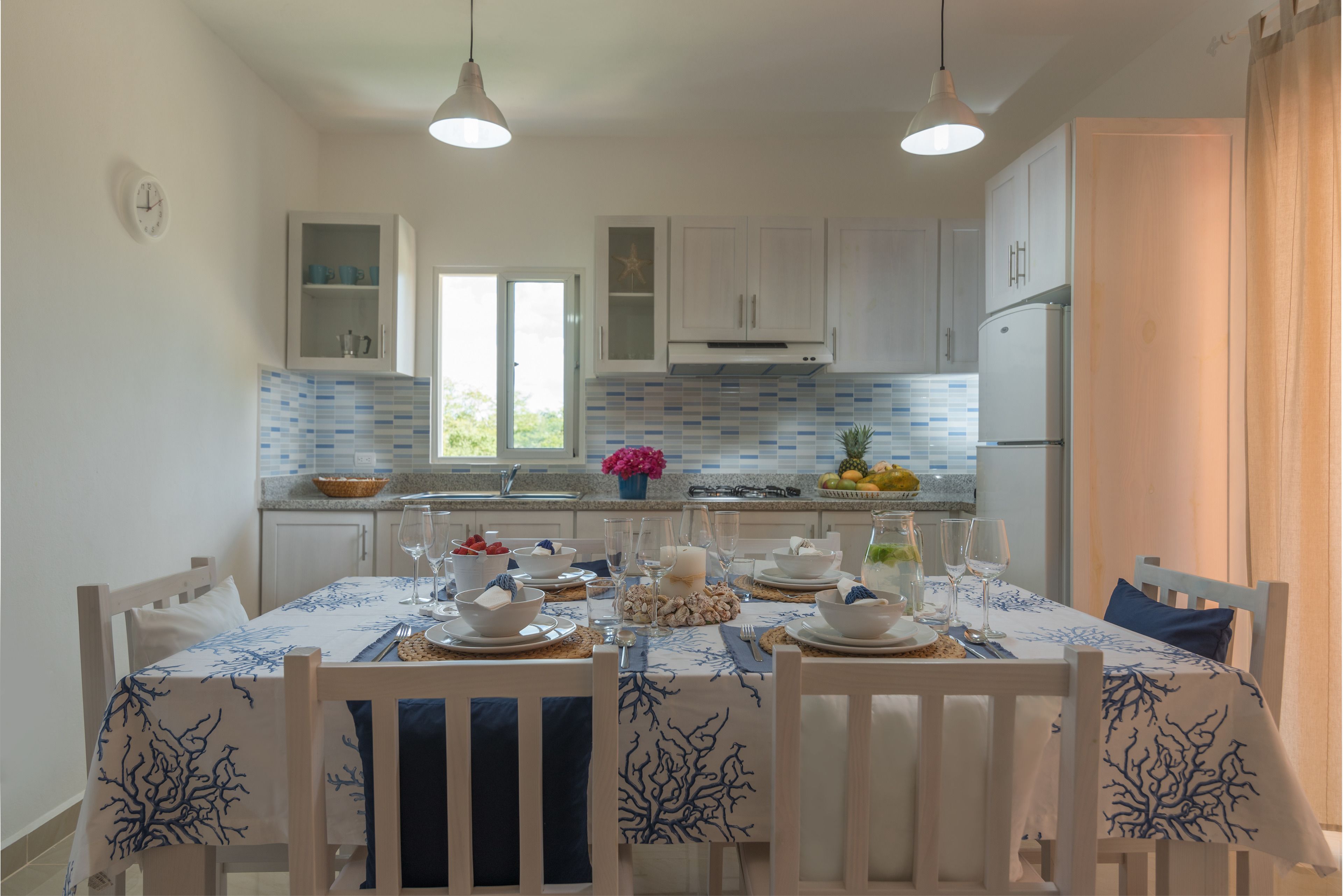 A modern kitchen with white cabinets, a tiled backsplash, and a dining area set for a meal.