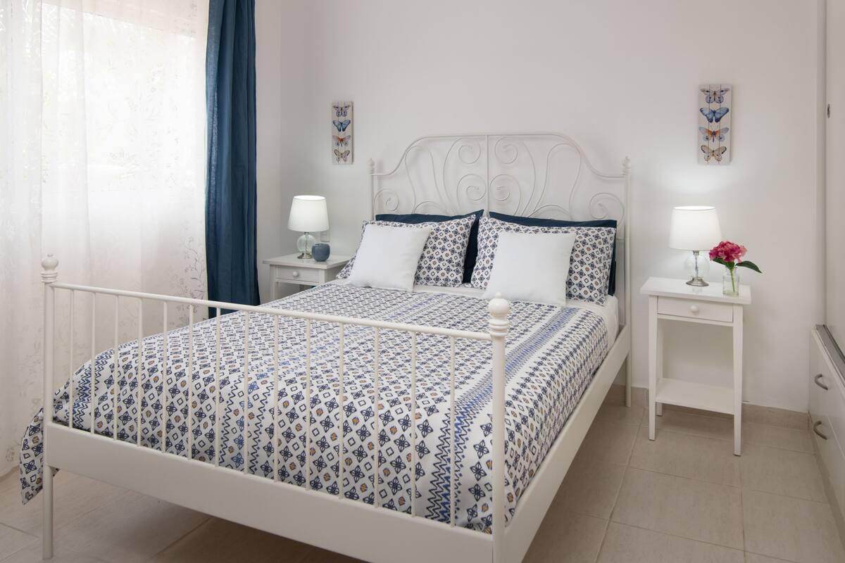 A neatly arranged bedroom with a bed, two bedside tables, and a window with curtains.