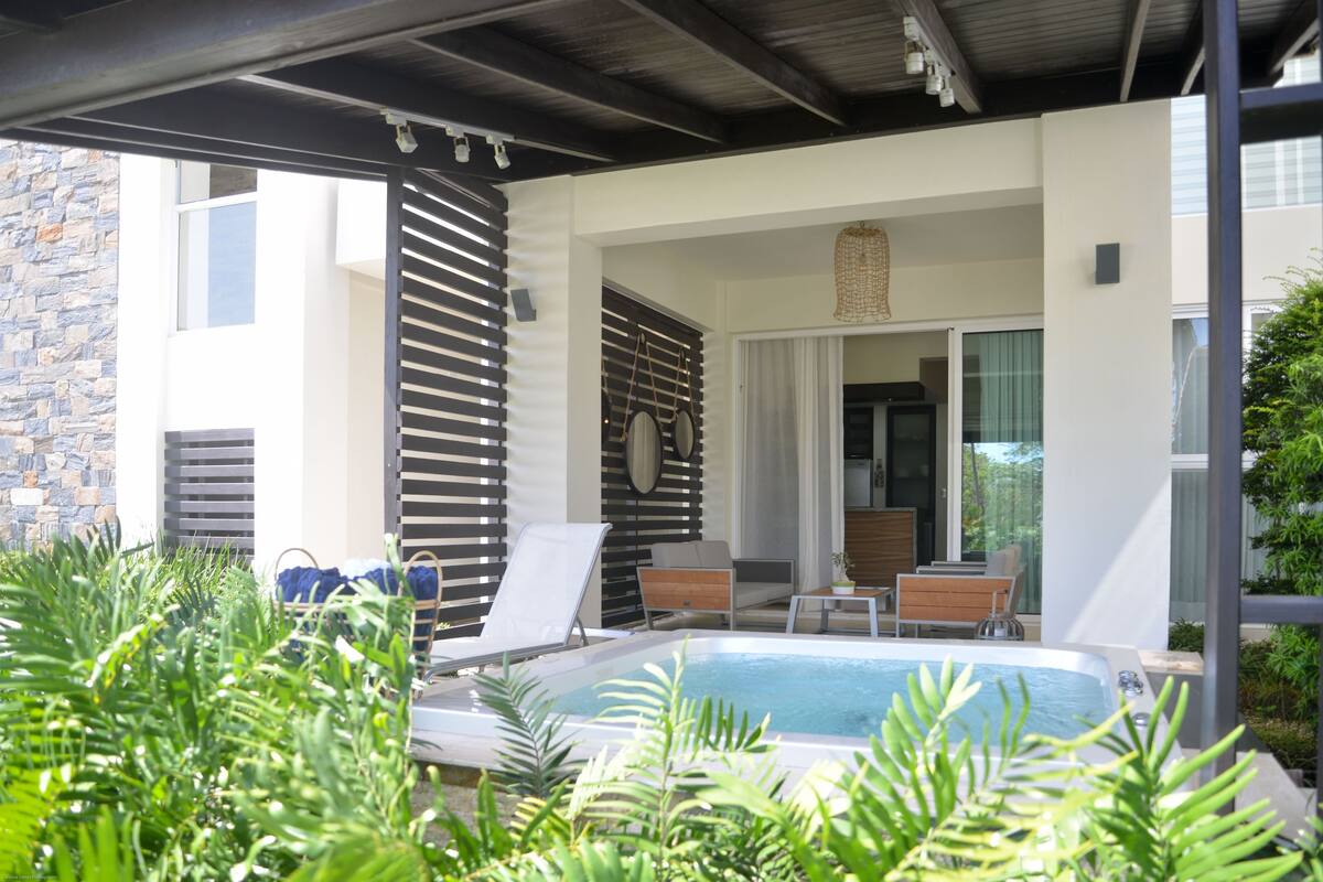 Un área de piscina moderna al aire libre con sillones reclinables, un jacuzzi y un muro de piedra.