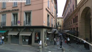 Une scène de rue à Bologne, en Italie, avec un bâtiment portant l’inscription « ASSICURAZIONI » et un panneau indiquant la « Via Oleari ».