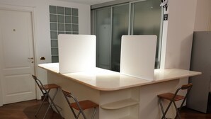 Une cuisine avec un plan de travail blanc, quatre tabourets de bar, un réfrigérateur et une porte portant un numéro.