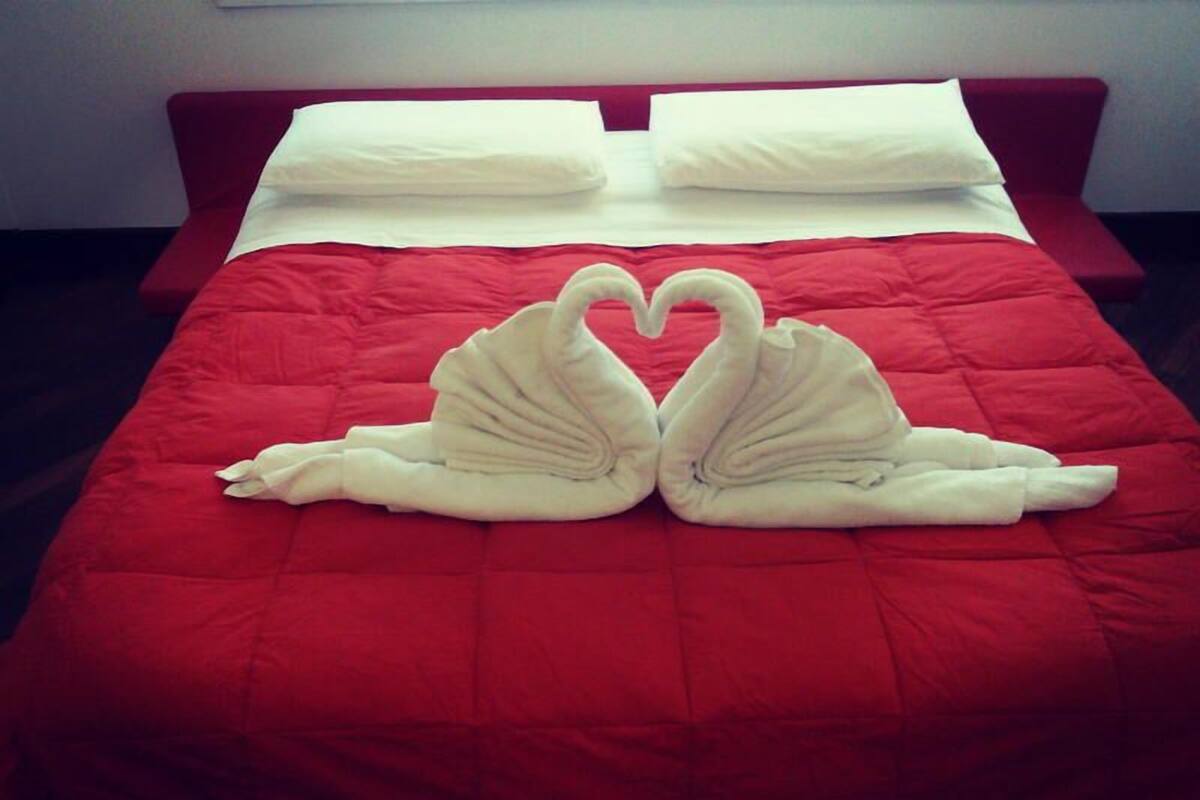 Een bed met een rode sprei en twee handdoeken in de vorm van zwanen.