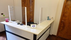 Un comptoir d’accueil avec un comptoir blanc, une enseigne indiquant le nom de l’hôtel, une caisse enregistreuse et une petite plante.