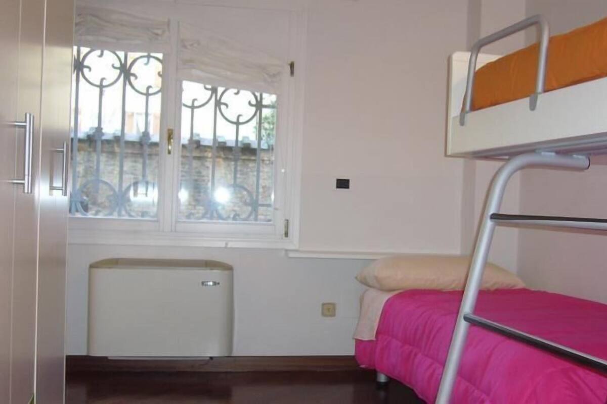 Een slaapkamer met een stapelbed, een raam, een radiator en een klein kastje.