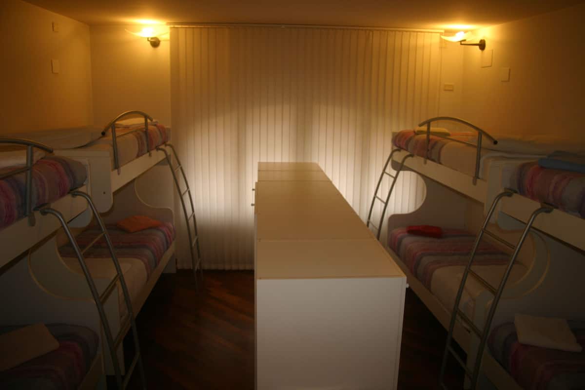 Een kamer met stapelbedden, een centrale tafel en twee wandlampen.