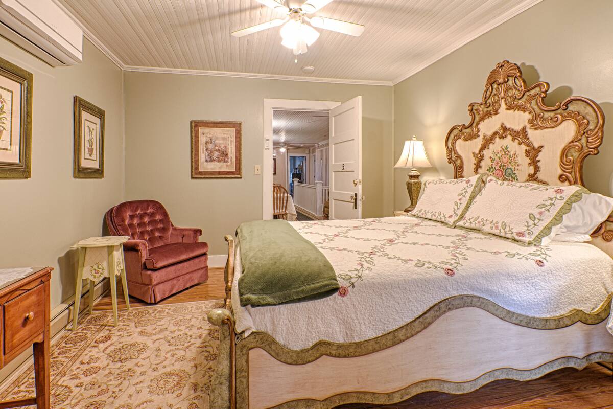 Un dormitorio con una cama grande, un sillón rojo, una mesita y un ventilador de techo.