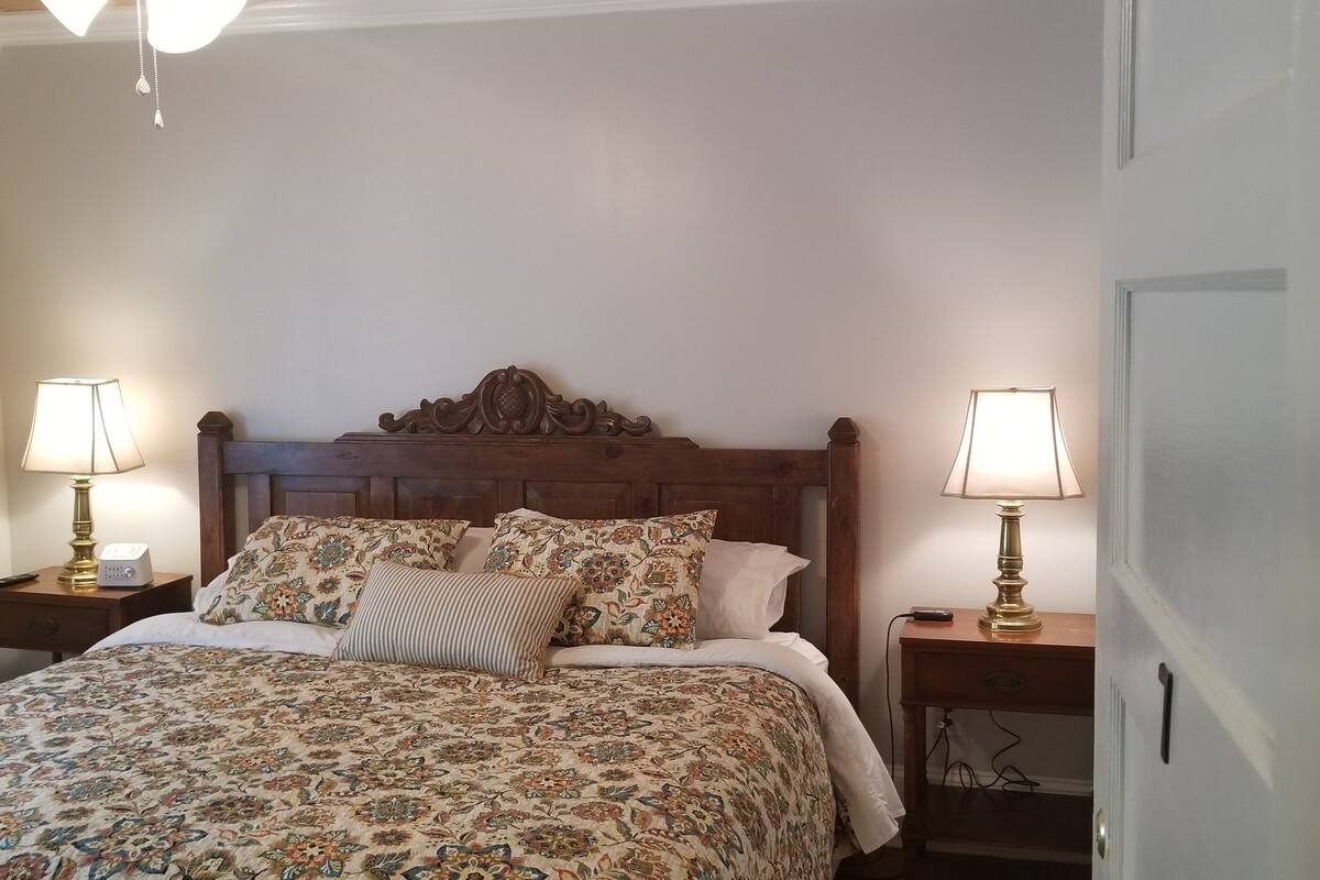 Una cama bien hecha con ropa de cama floral, dos lámparas de noche y un cabecero de madera.