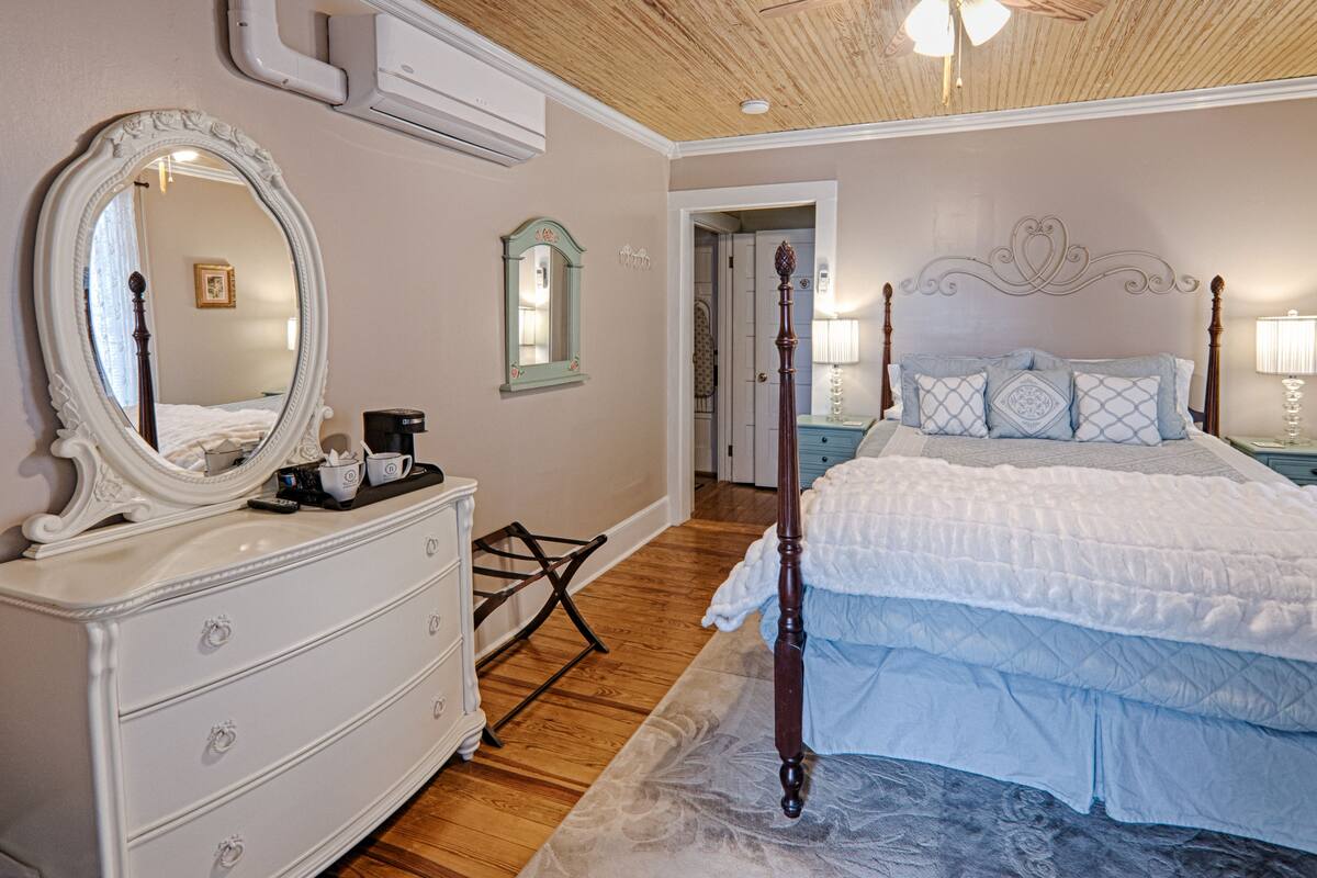 Un dormitorio con techo de madera, un aparador blanco con cajones, una cama grande con cabecero de madera y un espejo en la pared.