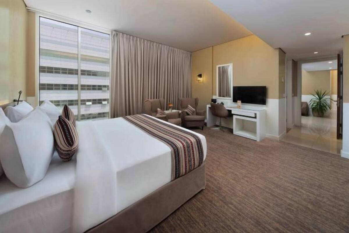 A hotel room with a large bed, a desk, a chair, a TV, and a window with curtains.