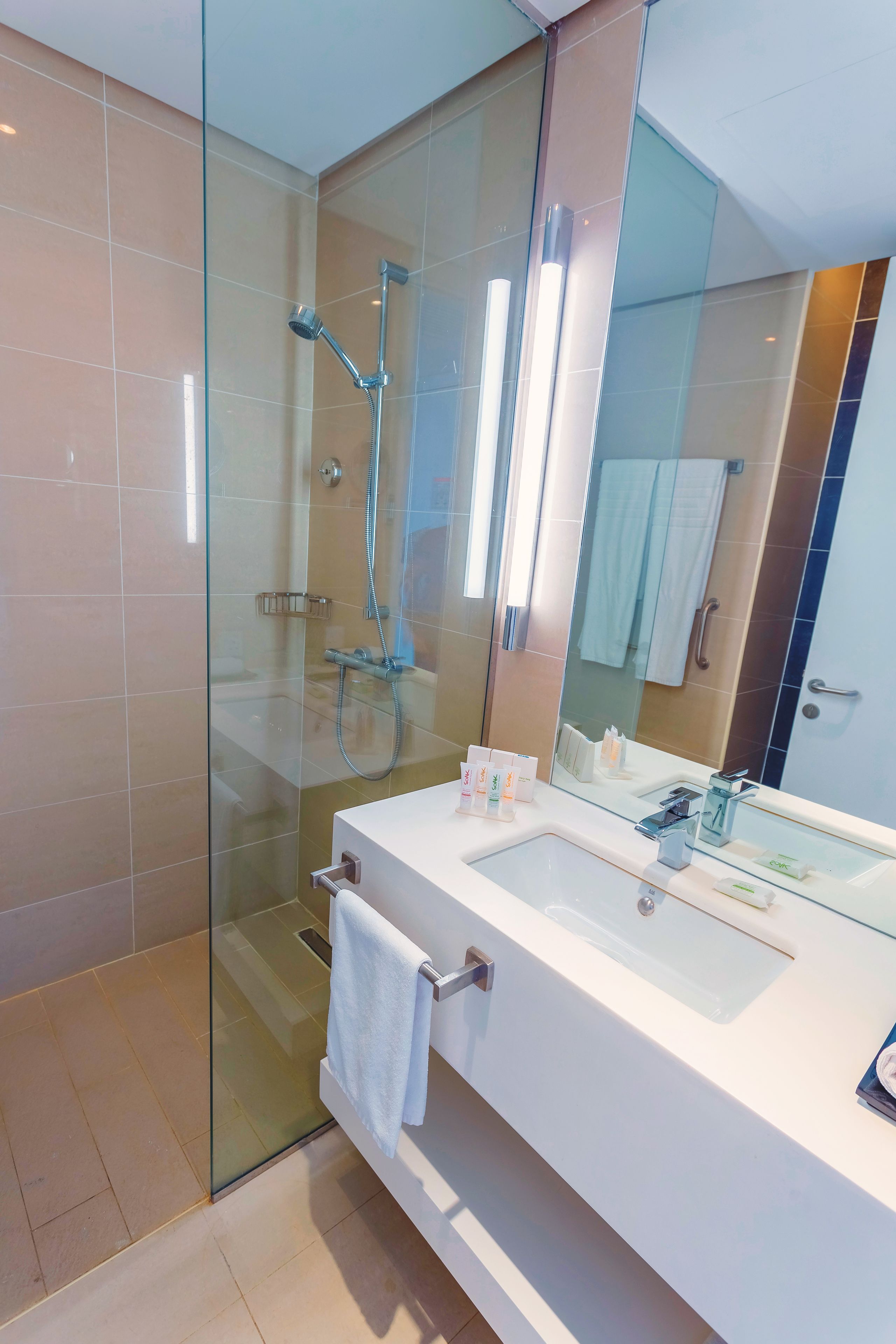 Un baño moderno con cabina de ducha de vidrio, tocador blanco con un espejo grande y un perchero para toallas.