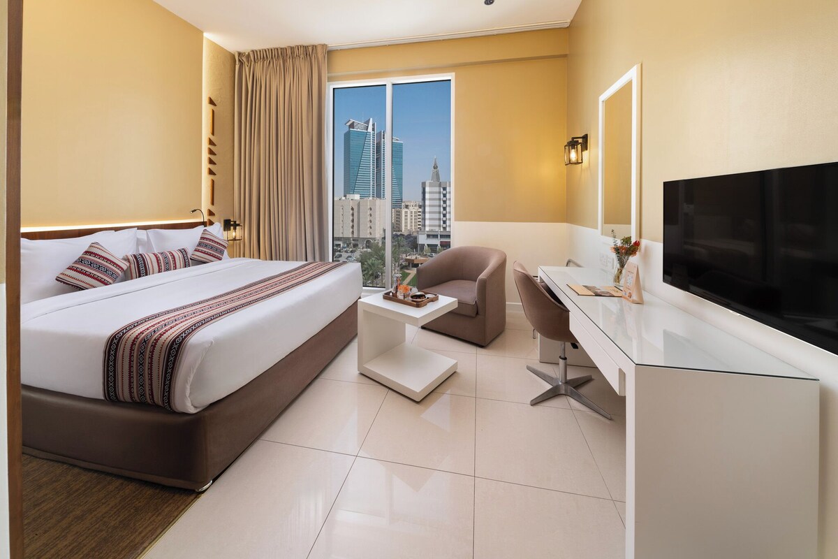 A hotel room with a bed, a desk, a chair, a TV, and a city view.