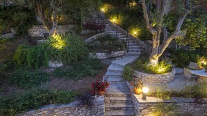 Un escalier en pierre, bordé d’une végétation luxuriante et de plantes en pot, qui monte une colline.