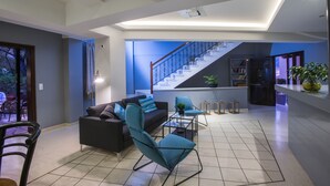 A modern living room with a sofa, armchairs, and a coffee table. A staircase leads to an upper level.