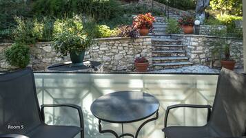 Un'area patio con un muro in pietra, piante in vaso e un tavolo in vetro con sedie.