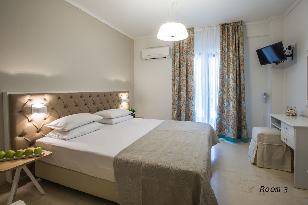 Ein ordentlich eingerichtetes Schlafzimmer mit einem großen Bett, einem Nachttisch mit Äpfeln, einem an der Wand montierten Fernseher und einem Schreibtisch mit einem Spiegel.