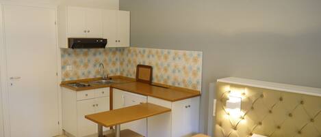 Quarto compacto com cama, mesa de cabeceira e uma pequena cozinha compacta com pia e armários.