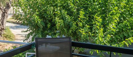 A balcony with a table and chairs, overlooking a lush green tree and a view of buildings in the distance.