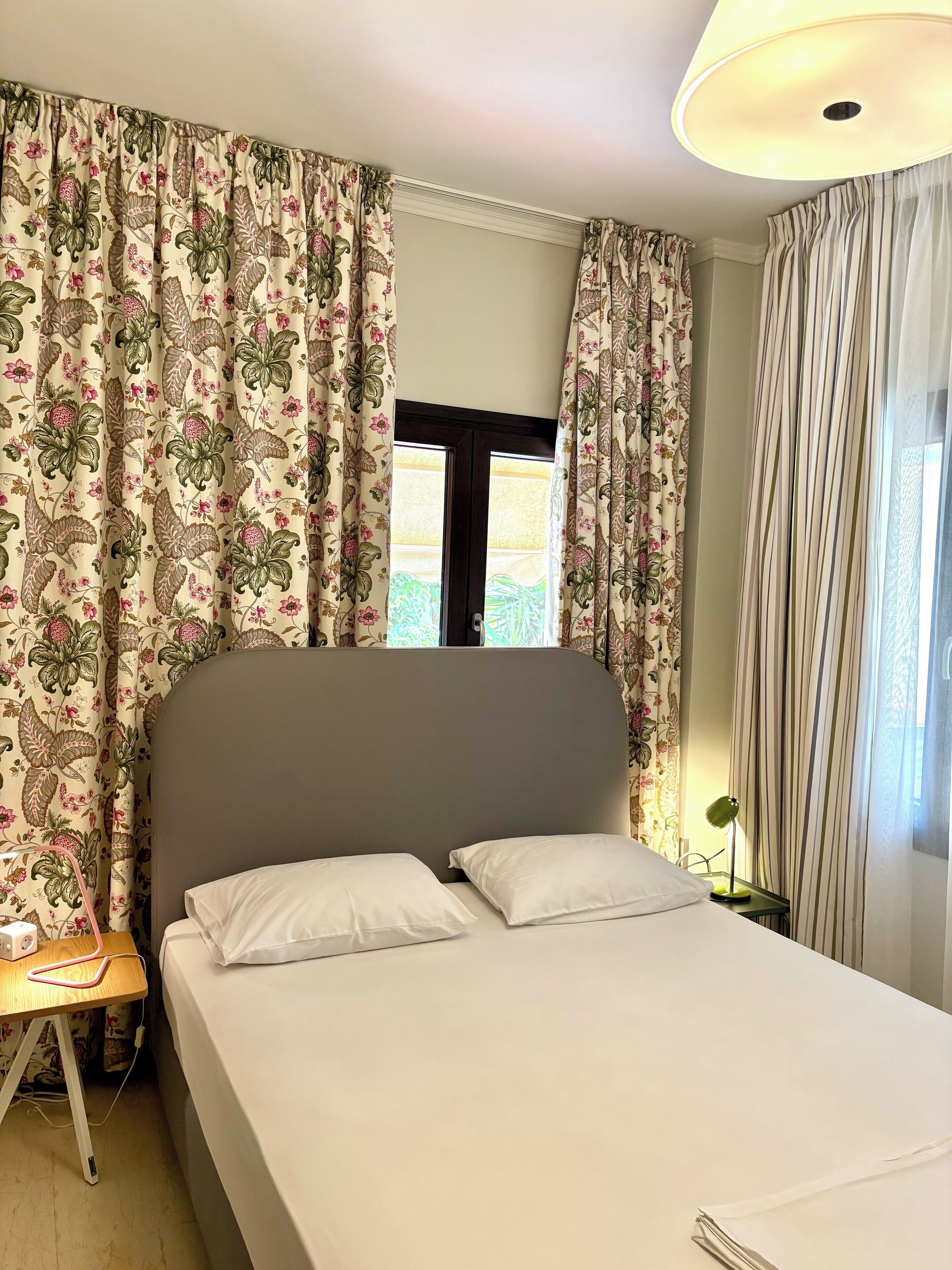 A bedroom with a bed, curtains, a bedside table, and a lamp.