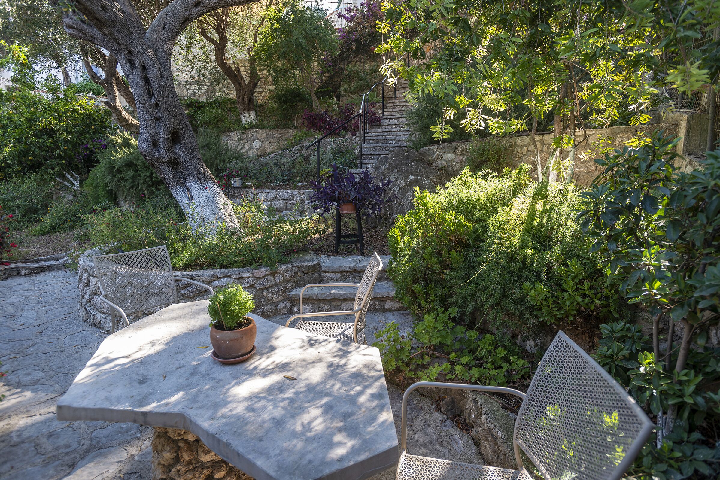 A stone patio with a table and chairs, surrounded by lush greenery and a stone wall.