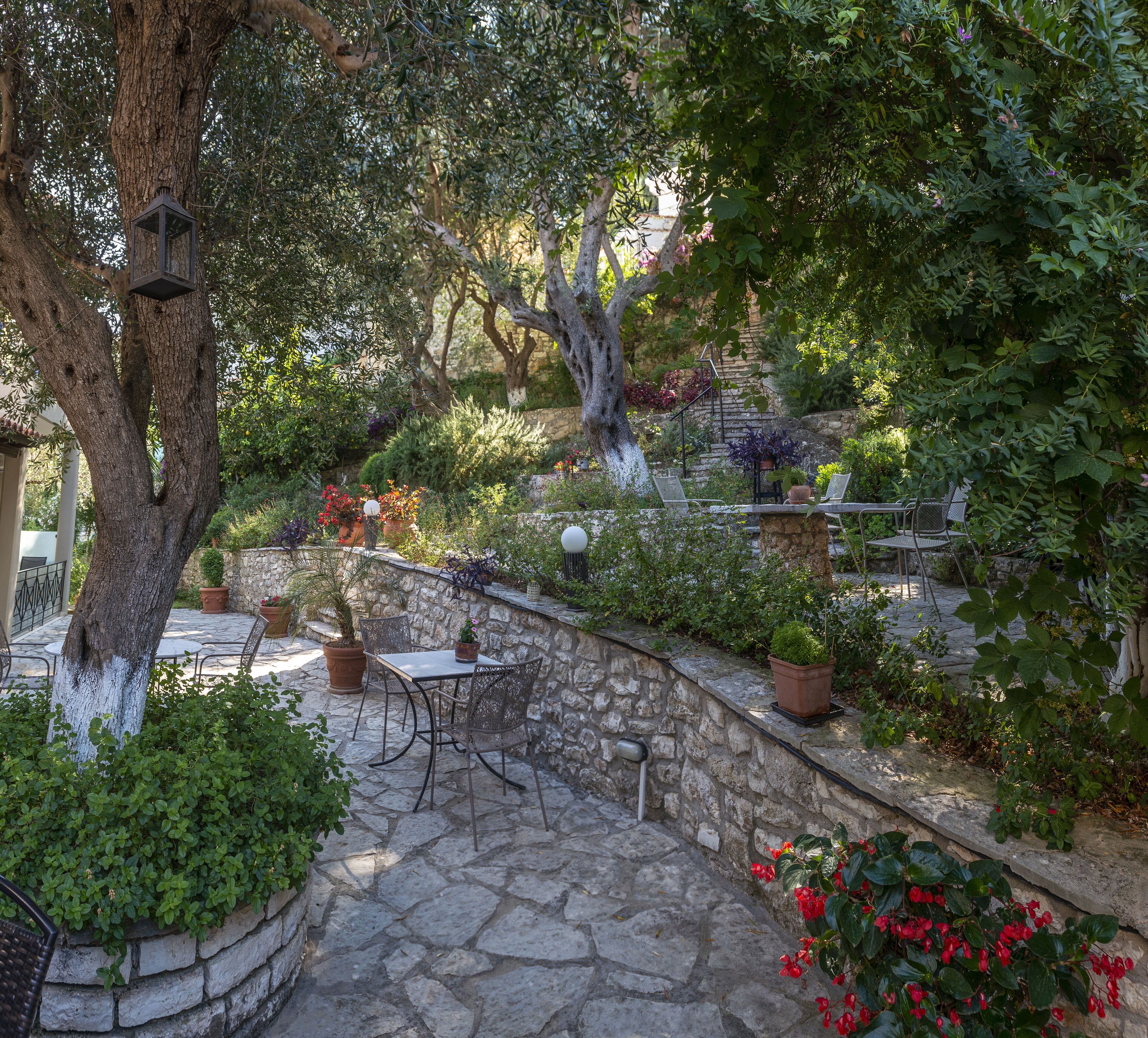 Une terrasse en pierre avec des sièges d’extérieur, entourée d’une végétation luxuriante et de plantes en pot.
