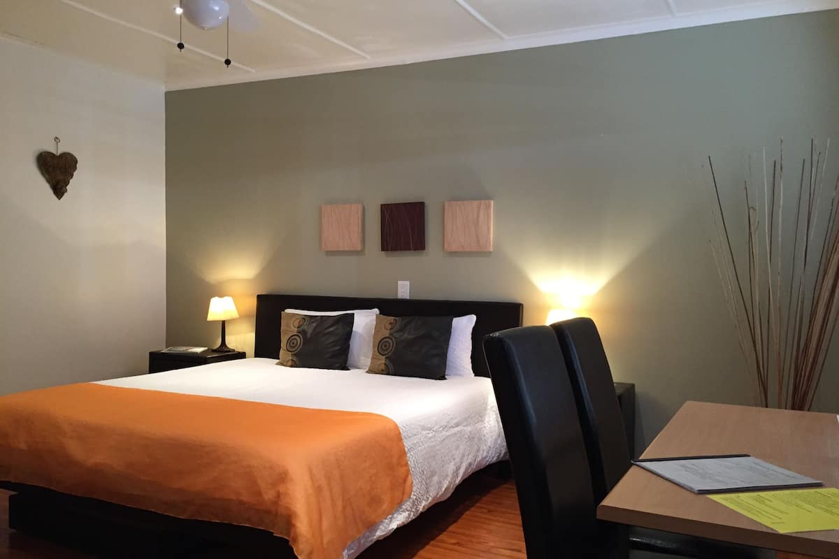 Habitación de hotel con cama, mesitas de noche con lámparas, un escritorio con silla y cuadros colgados en la pared.