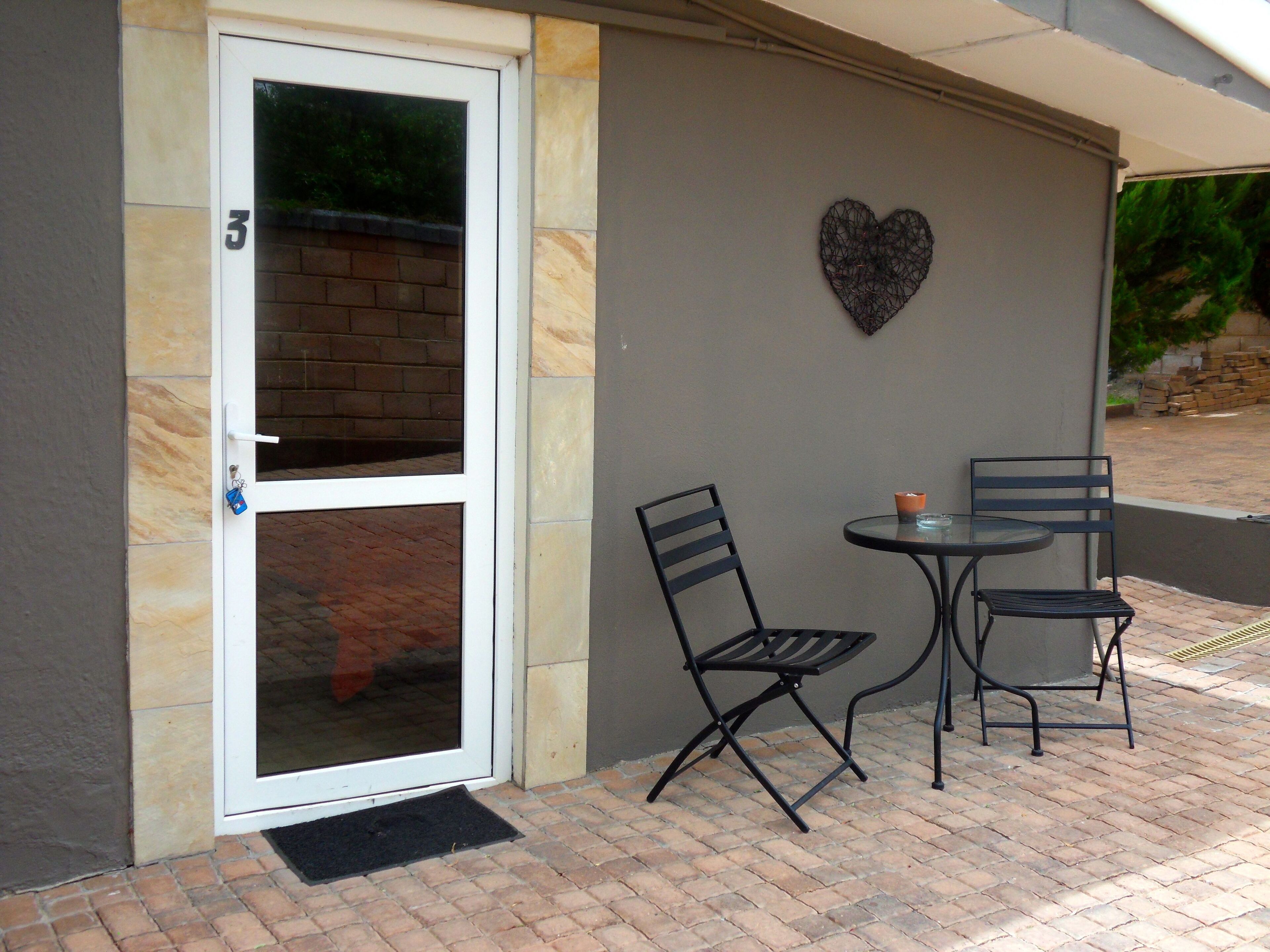 A door with a glass panel, a heart-shaped decoration on the wall, and two chairs with a table.