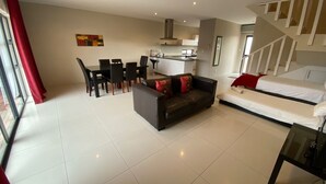 Una sala moderna con sofá, mesa de comedor, sillas y una cocina al fondo.