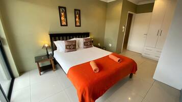 Habitación de hotel con una cama grande, una mesita de noche, un armario y dos marcos con cuadros colgados en la pared.