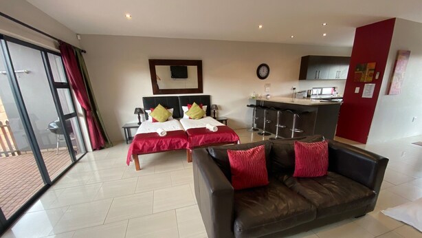 Habitación de hotel con dos camas, un sofá, una zona de cocina y una puerta corrediza de cristal al exterior.