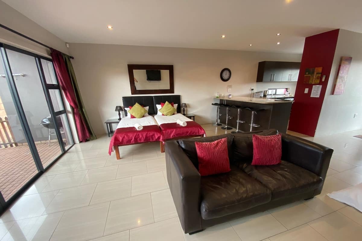Habitación de hotel con dos camas, un sofá, una zona de cocina y una puerta corrediza de cristal al exterior.