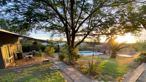 Un patio trasero con piscina, un porche con mobiliario exterior y un gran árbol que da sombra.