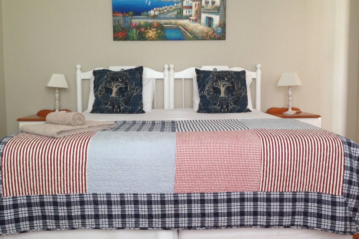 Quarto com cama, duas almofadas, um quadro e mesa de cabeceira com abajur.