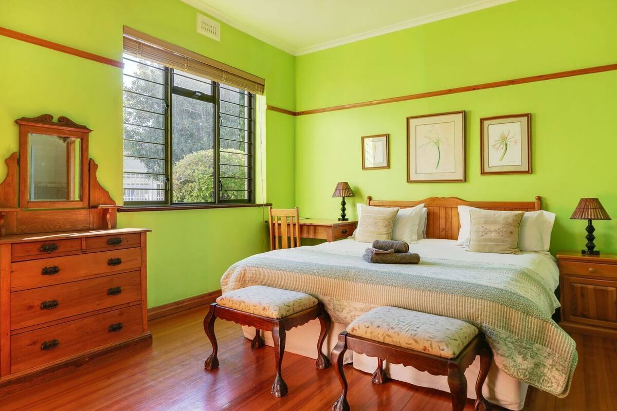 Quarto com cama, cômoda de madeira e janela com persianas.