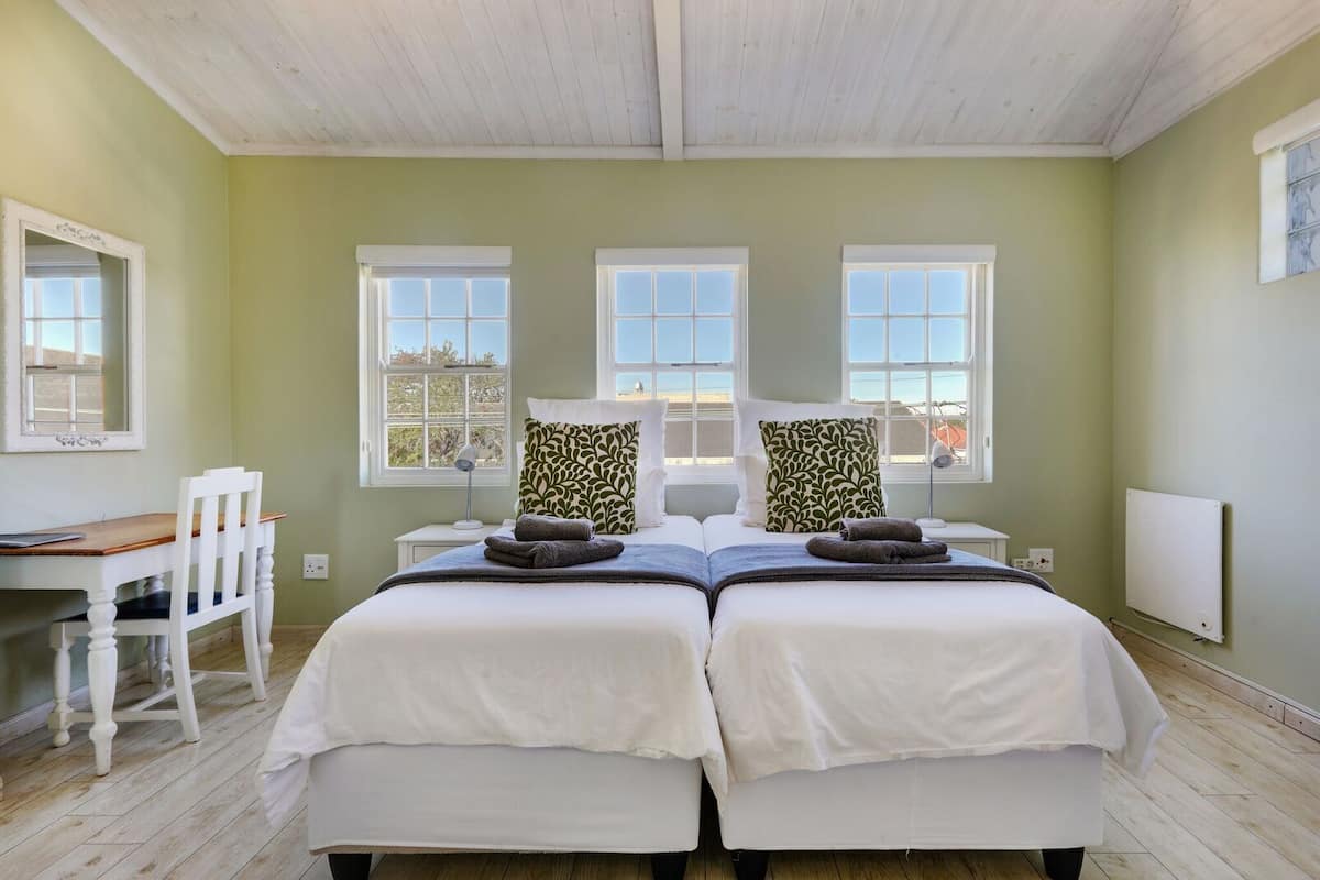 Uma cama de casal com duas almofadas, uma mesa de trabalho com cadeira e uma janela com vista.