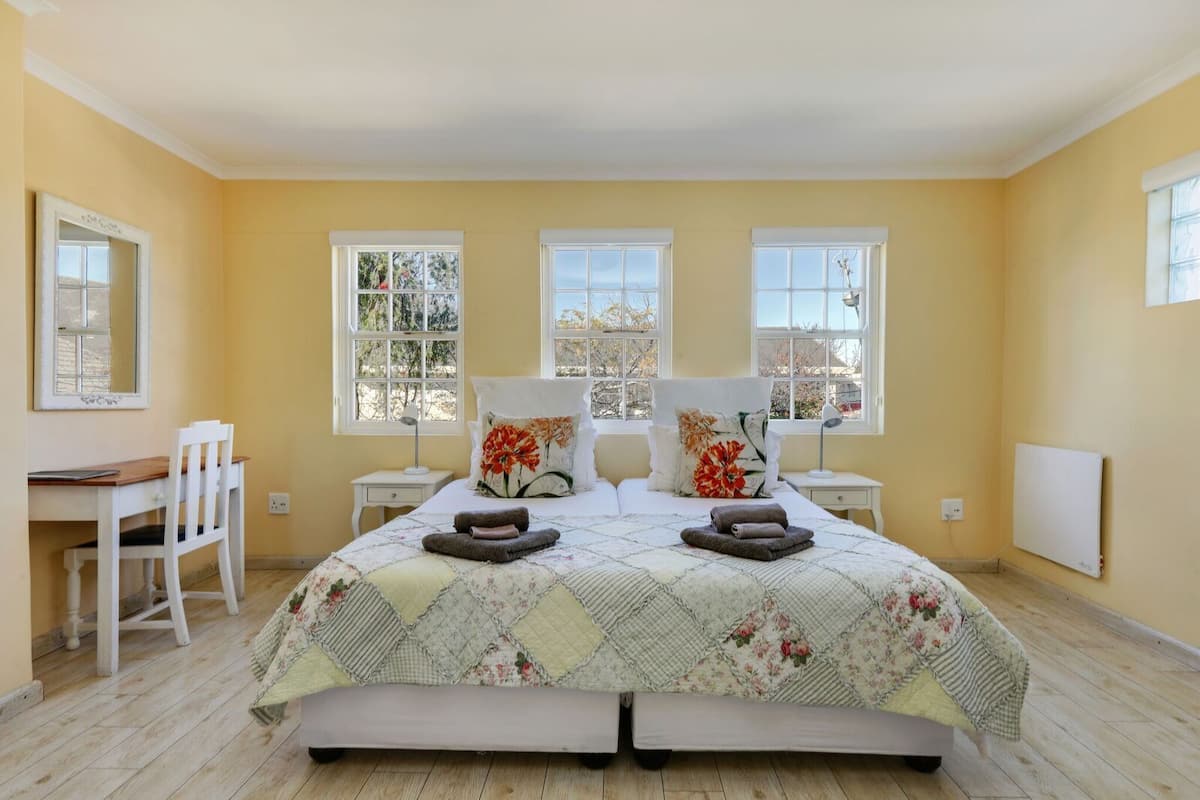 Quarto com cama grande, duas mesas de cabeceira, escrivaninha e uma cadeira.
