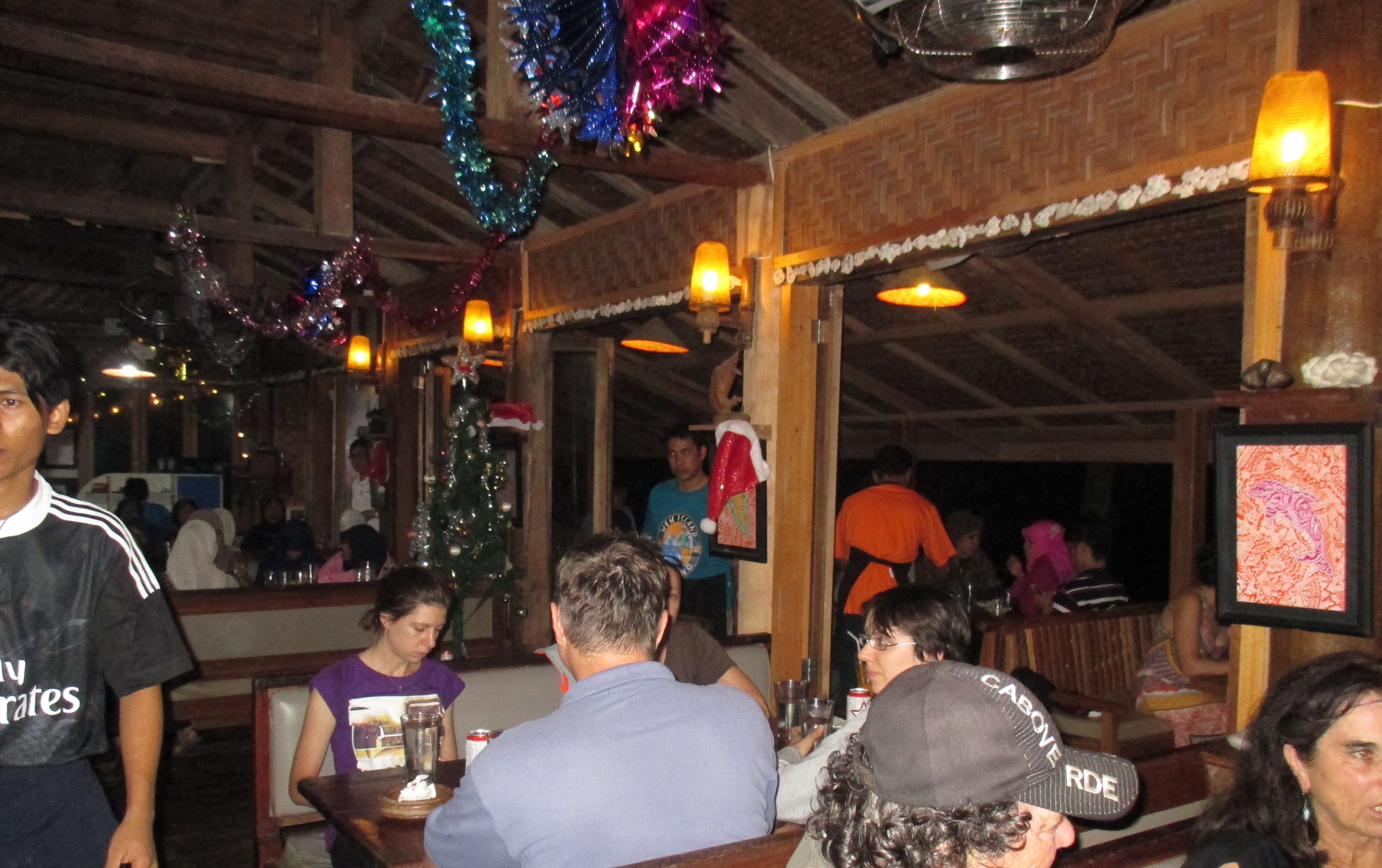 A restaurant interior with wooden beams, festive decorations, and patrons seated at tables.