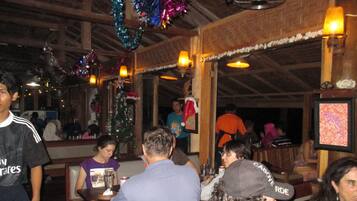 A restaurant interior with wooden beams, festive decorations, and patrons seated at tables.
