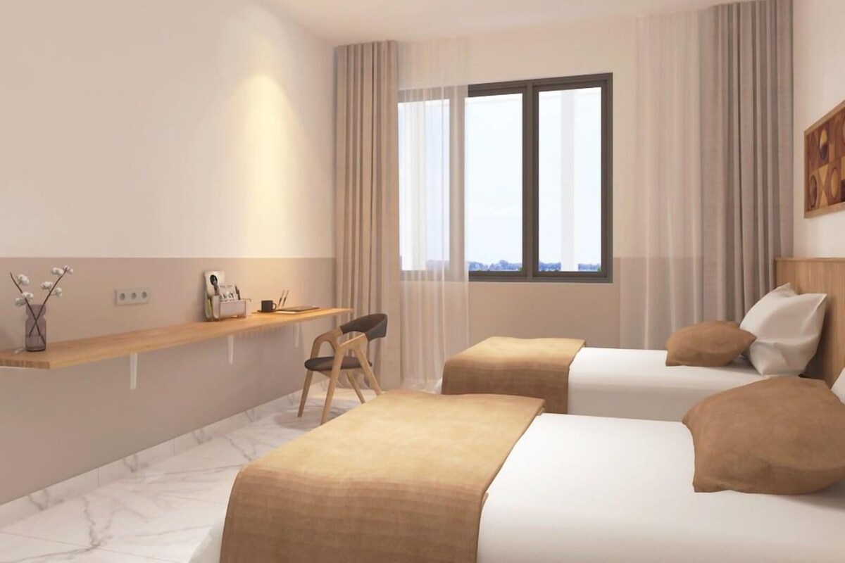 A hotel room with two beds, a desk, a chair, and a large window.