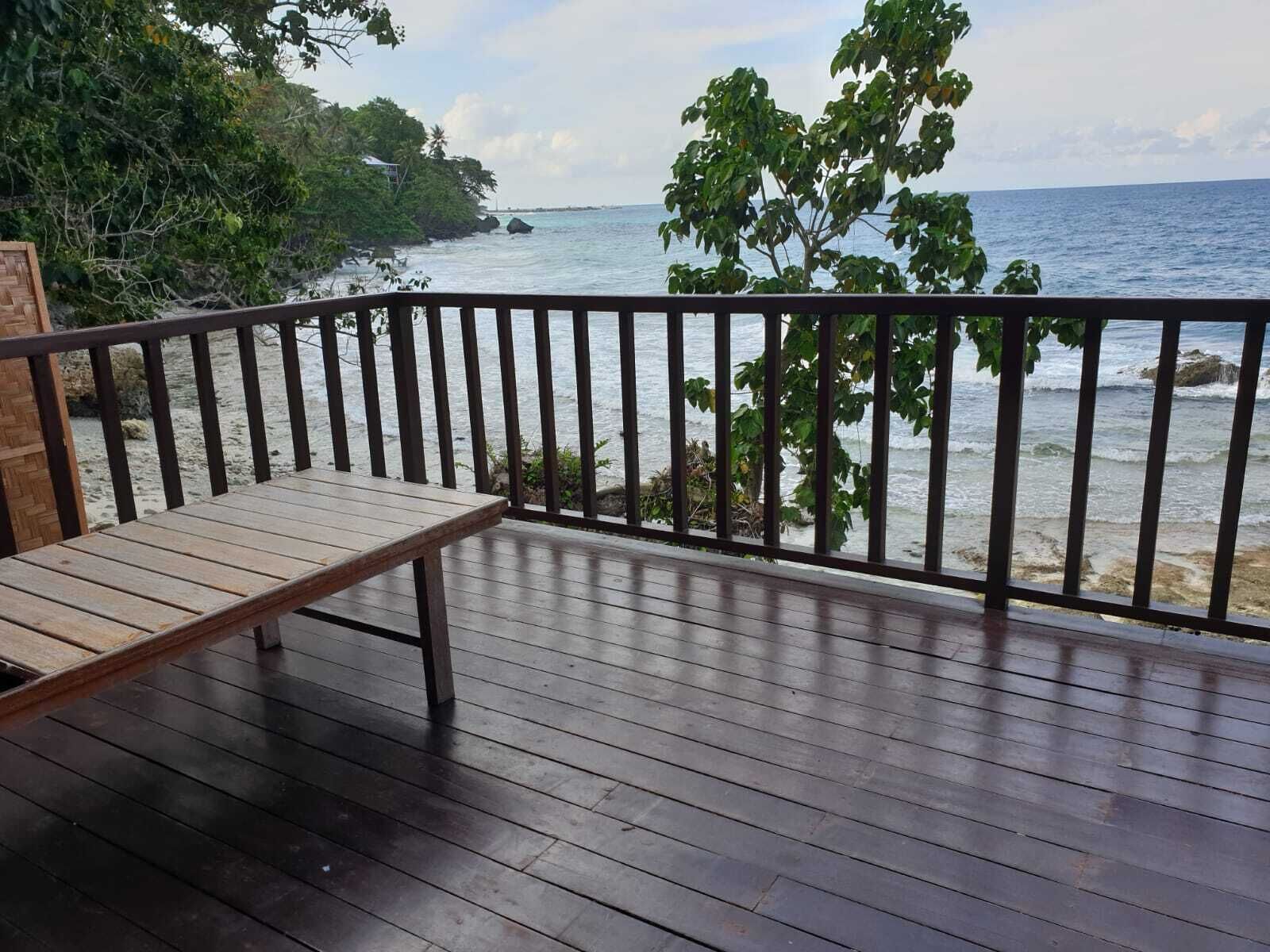 Une terrasse en bois avec un banc donnant sur une plage bordée de rochers et d’arbres.