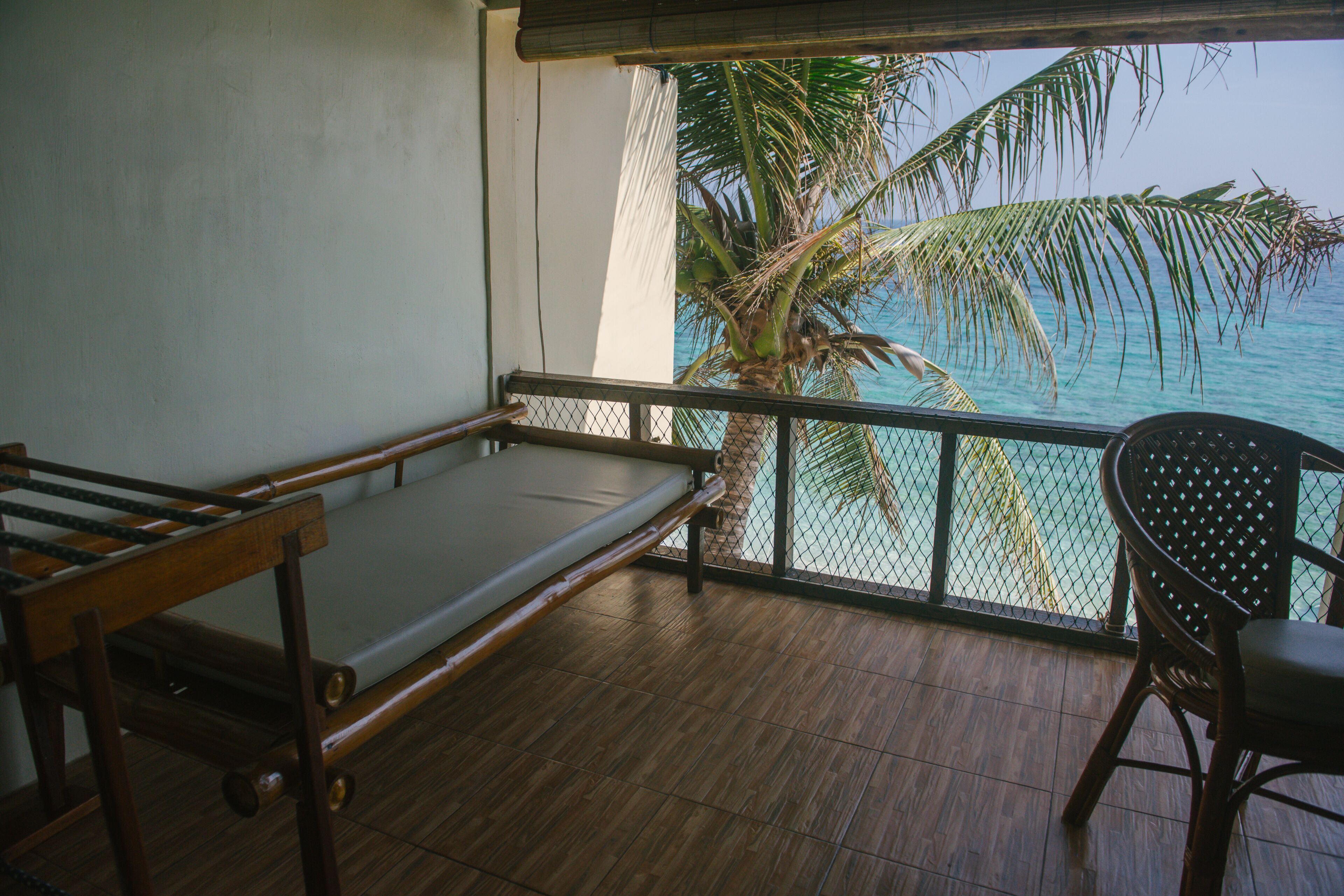 A balcony with a wooden bench, a chair, and a view of the ocean and palm trees.