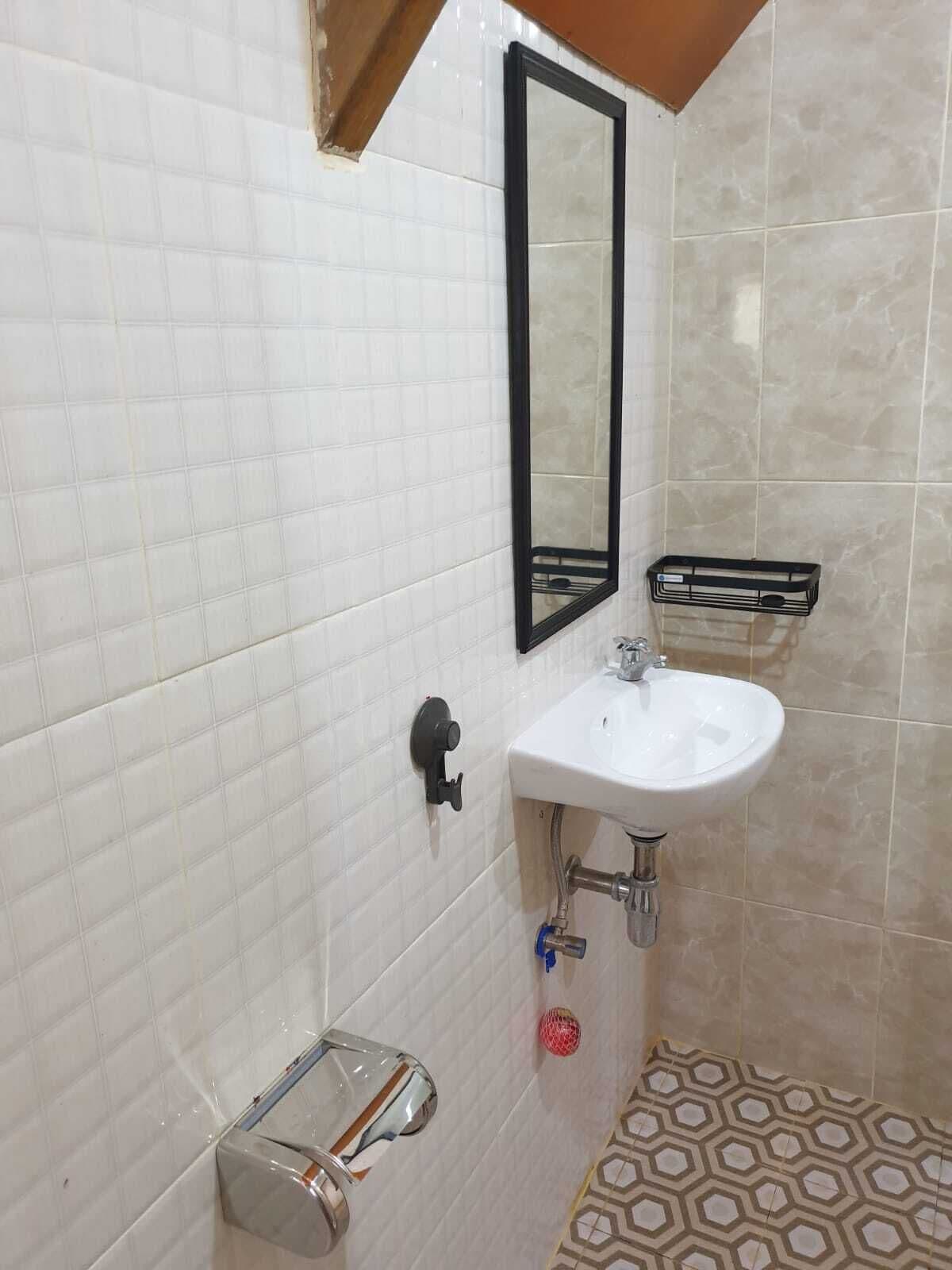 A bathroom with white tiled walls, a white sink, a black-framed mirror, a towel rack, and a patterned floor.