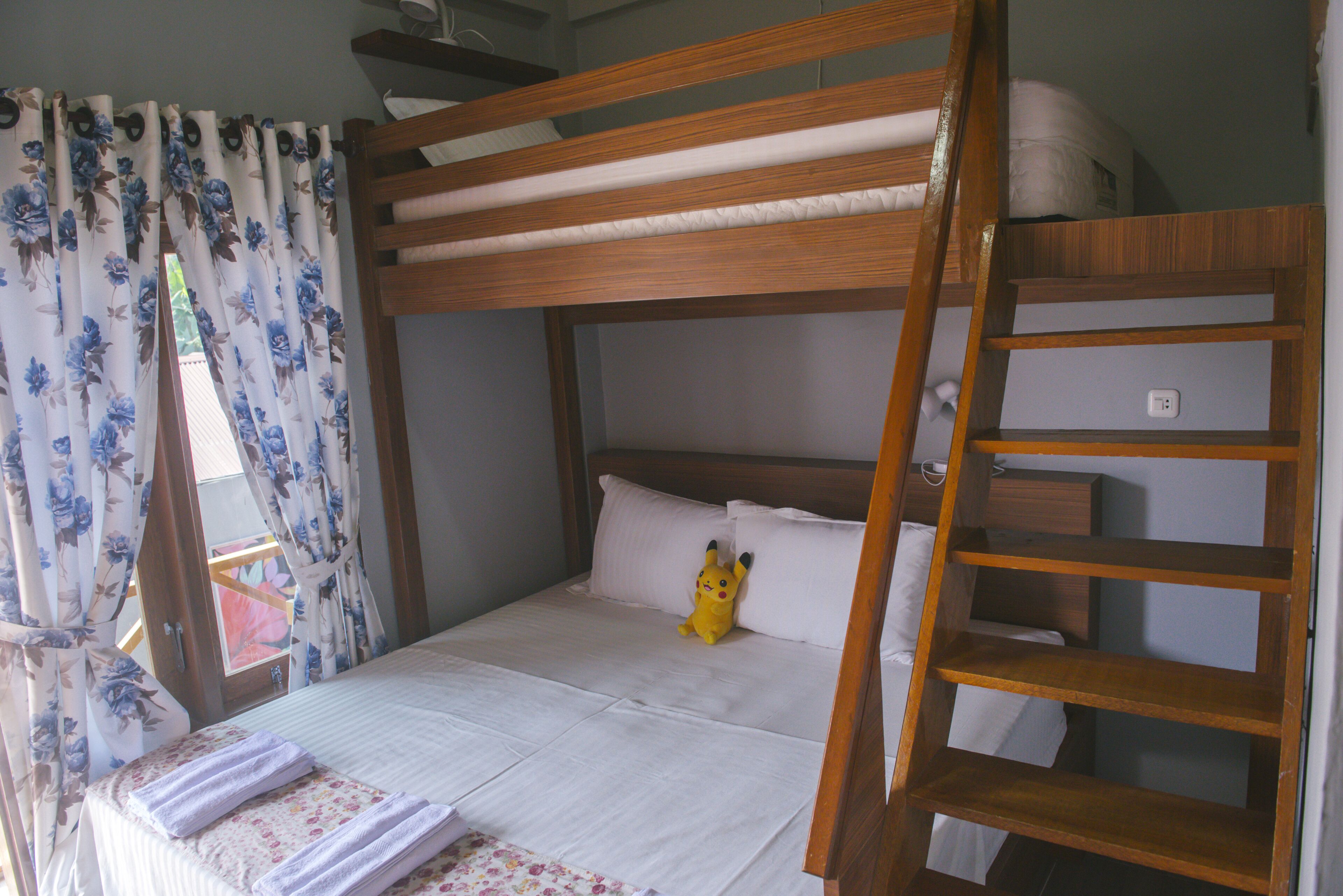 Un lit superposé avec une échelle en bois, un matelas blanc et un doudou à l’effigie de Pikachu sur le lit du bas.