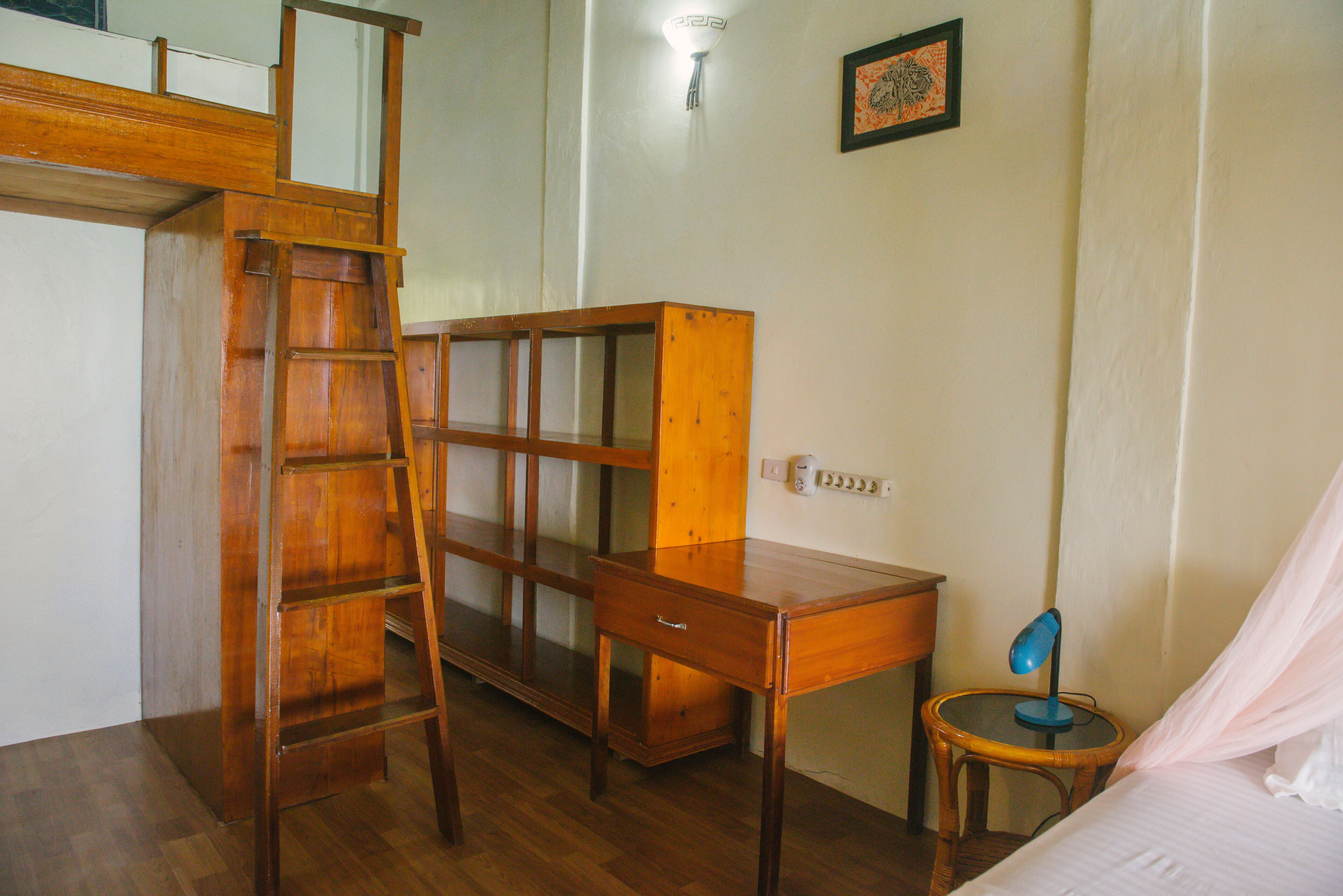 A room with a wooden desk, a ladder, a chair, a bedside table, and a bed with a canopy.