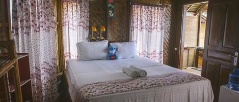 Un dormitorio de madera con una cama grande, cortinas florales y una pequeña mesa con lámpara.