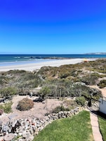 Un paisaje costero con playa arenosa, terreno rocoso y vegetación escasa.