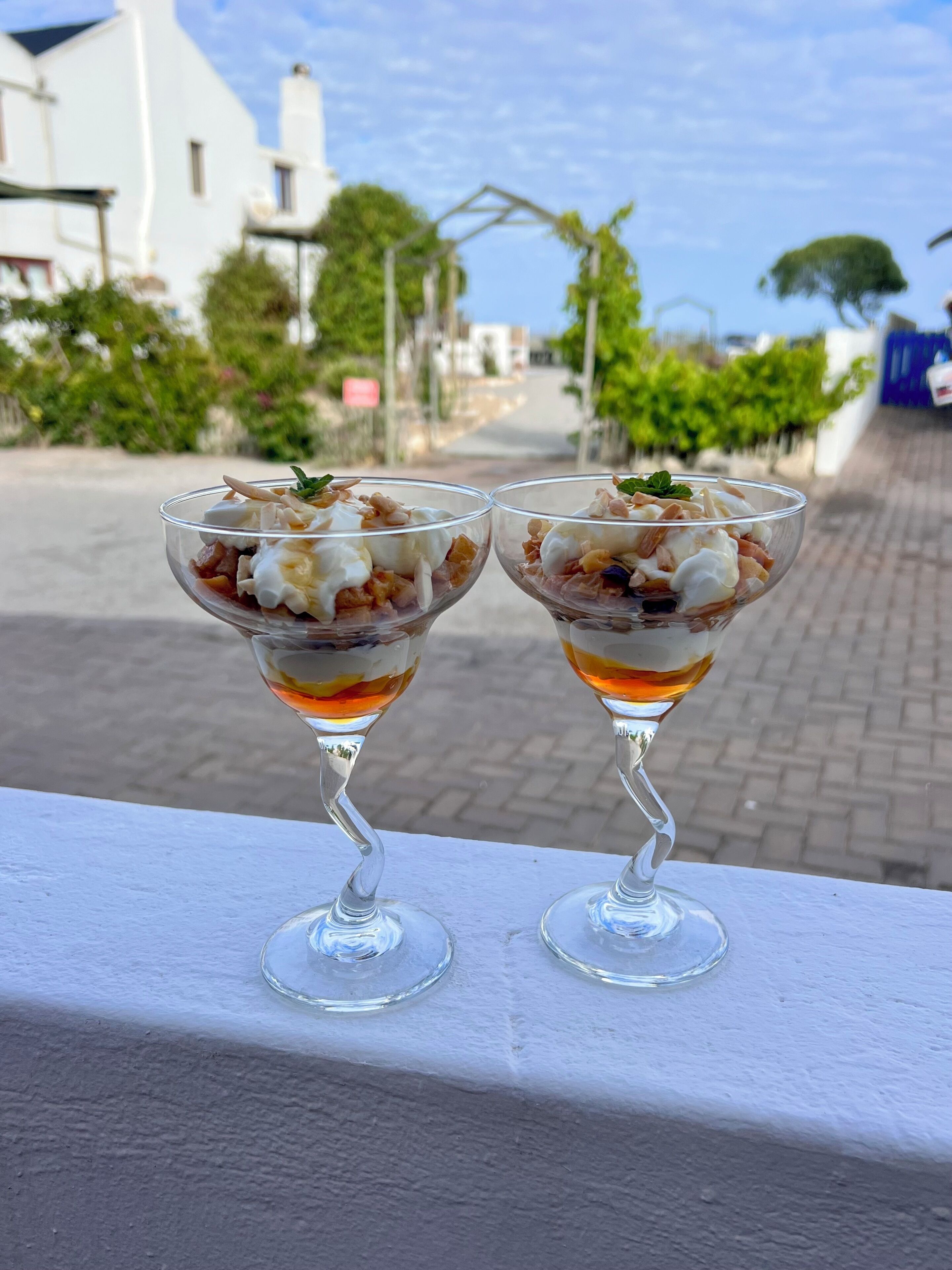 Two dessert glasses on a white ledge with a street view in the background.